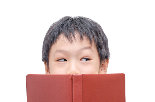 A boy peaking out from above a book.