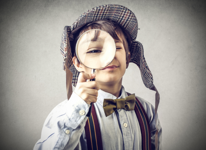 child in detective hat looking through magnifying glass