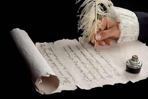 A hand writing on a scroll with a quill.