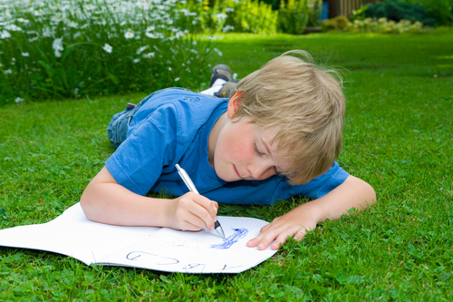 A boy writing whilst lying on grass.